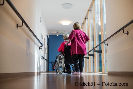 Frau schiebt eine Pflegebedürftige Seniorin durch einen Flur