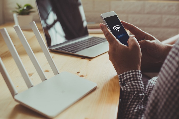 Die Signalstärke ist zuständig für die Geschwindigkeit und Effizienz der Internetverbindung. Sie hat wesentlichen Einfluss auf die Nutzung und kann durch individuelle Einstellungen stark beeinflusst werden. Mann richtet mit Handy und Laptop sein WLAN ein