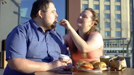 Todsünde Völlerei, das Gierige in sich hineinstopfen kann auch krankheitsbedingt sein Eine dicke Frau füttert einen noch dickeren Mann mit Pommes und Burgern