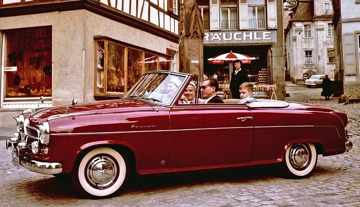 Ein weinrotes Borgward Cabriolet fährt über einen alten Stadtplatz