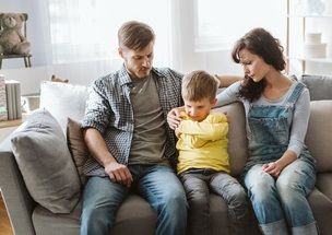 Eltern sitzen mit traurigem Sohn auf der Couch und trösten ihn