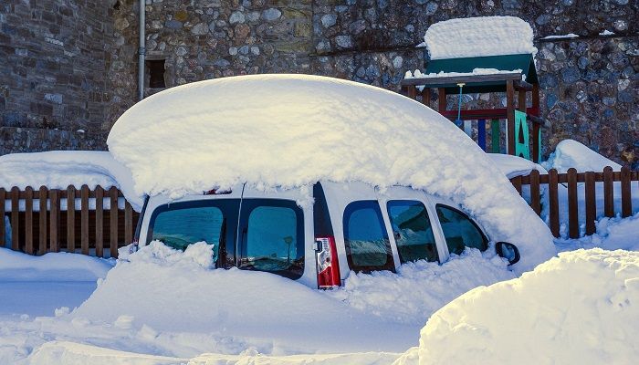 Auto ist total eingeschneit und steht vor einem Spielplatz