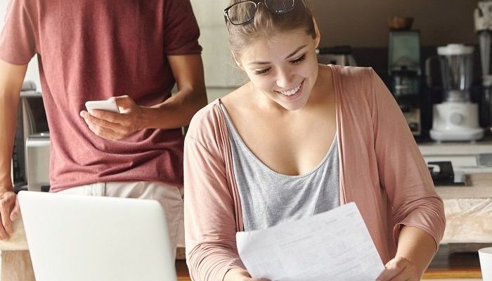 Frau vor einem Laptop und Rechner, freut sich mit einem Blatt Papier in der Hand