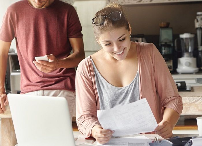 Frau vor einem Laptop und Rechner, freut sich mit einem Blatt Papier in der Hand