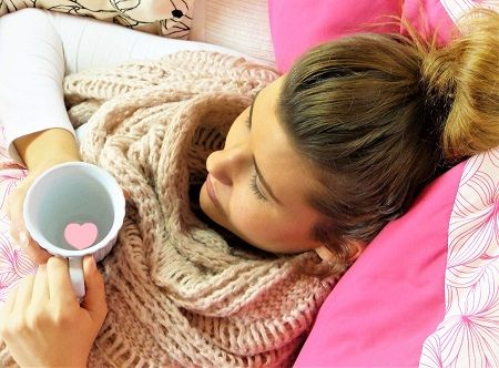 Frau liegt mit einem Becher Tee auf dem Sofa