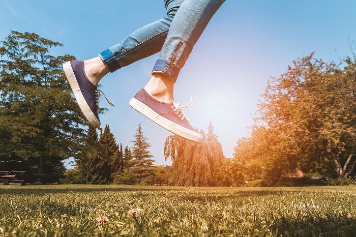 Bequeme und modisch Schuhe müssen sich heutzutage nicht mehr ausschließen Frau springt im Park hoch, man sieht Ihre bequemen Schuhe