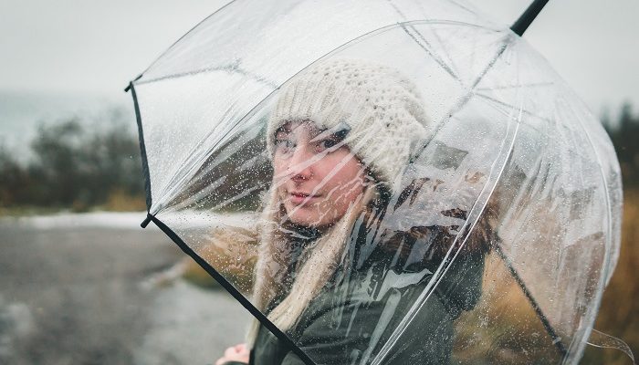 Junge Frau steht mit transparentem Schirm im Regen