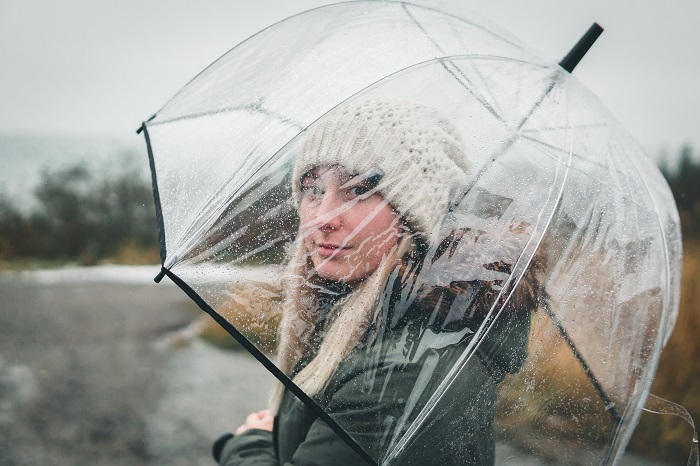 Junge Frau steht mit transparentem Schirm im Regen