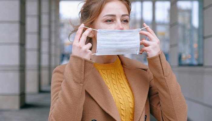 Frau steht in einer Stadt und legt gerade einen Mundschutz an