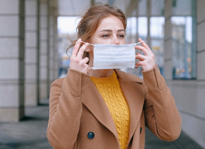 Frau steht in einer Stadt und legt gerade einen Mundschutz an