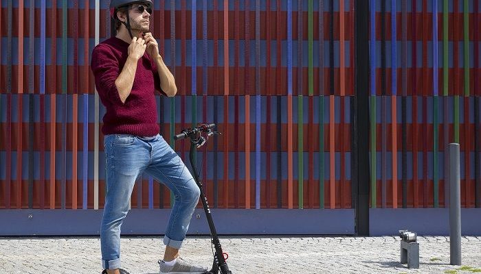 Junger Mann steht mit seinem E-Scooter auf einer Strasse