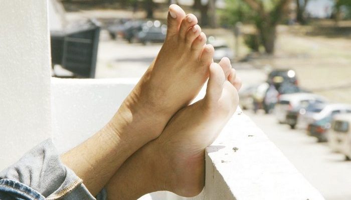 Zwei Füße liegen relaxed auf einer Balkonbrüstung
