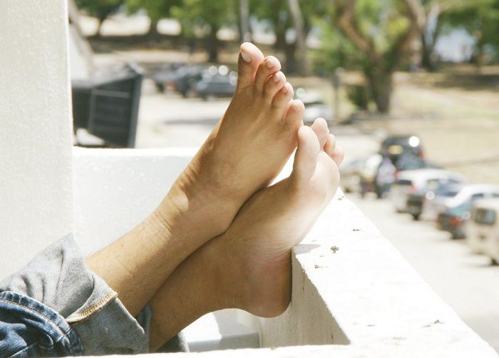 Zwei Füße liegen relaxed auf einer Balkonbrüstung