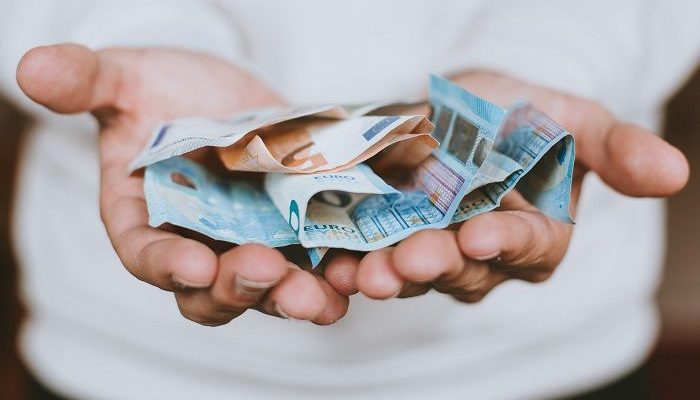 Männerhände halten mehrere Euro Geldscheine offen hin