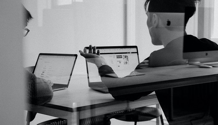 Junge Männer sitzen, mit Laptops vor sich, in einem Büro und recherchieren im Internet
