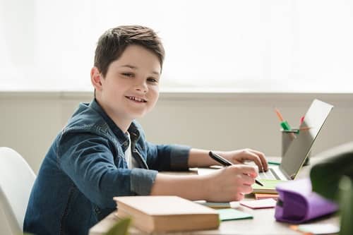 Junge sitzt über Schulsachen vor einem Laptop