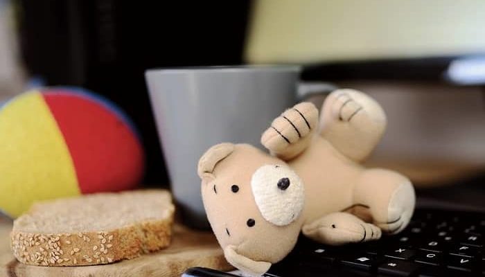 Ein umgefallener Teddy liegt auf einer Computertastatur, daneben ein Brot und ein Kaffeebecher