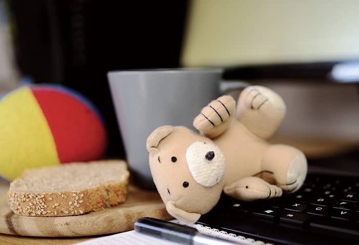 Ein umgefallener Teddy liegt auf einer Computertastatur, daneben ein Brot und ein Kaffeebecher