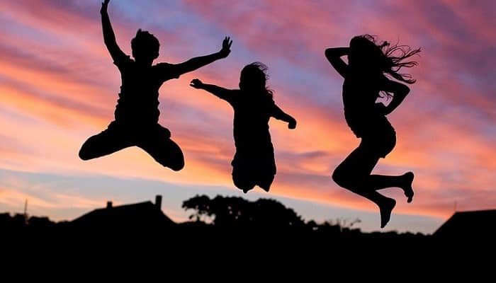 Drei Kinder springen im Abendrot Trampolin im Garten