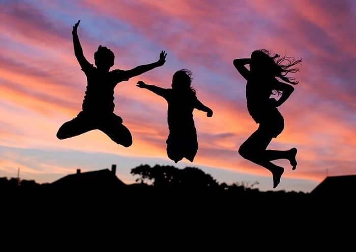 Drei Kinder springen im Abendrot Trampolin im Garten