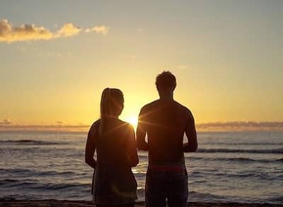 Ein Paar sieht vom strand aus in den Sonnenuntergang und spricht miteinander