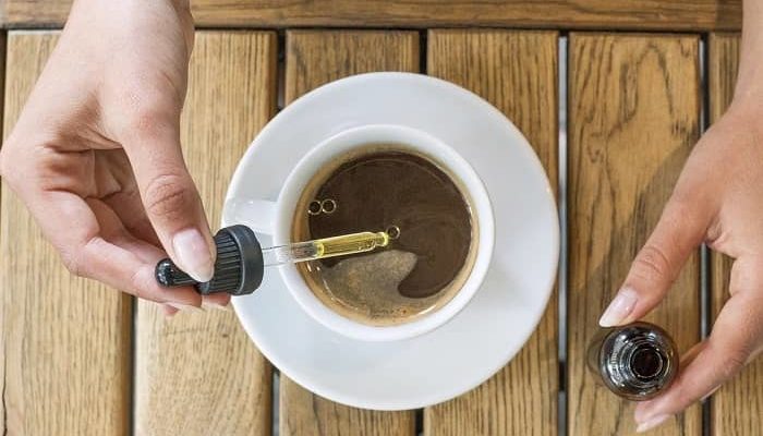 eine Frau tropft CBD Öl in Ihren Kaffee