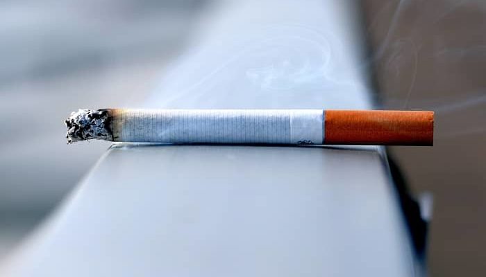 Eine rauchende Zigarette liegt auf einem Brückengeländer