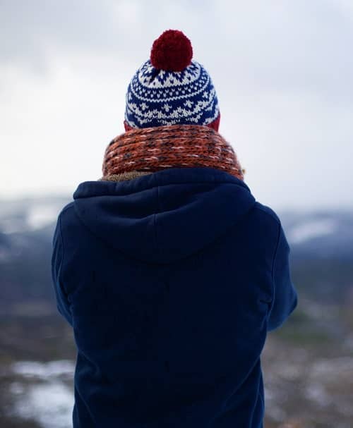 Frau steht warm angezogen auf einem Berg und schaut auf eine gegenüberliegende Bergkette