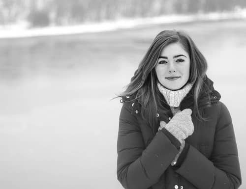 Frau steht mit Winterjacke im Freien an einem Fluss