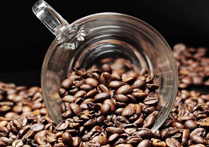 Eine Glastasse liegt in einem großen Berg Kaffeebohnen