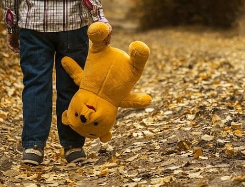 Kind geht traurig mit seinem Teddy auf einem Waldweg