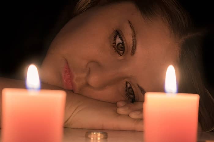 Traurige Frau liegt mit dem Kopf auf dem Tisch, vor einem Ring und zwei Kerzen