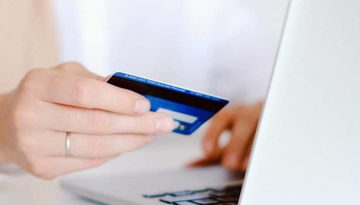 Frau sitzt vorm Laptop und bezahlt dabei mit Kreditkarte