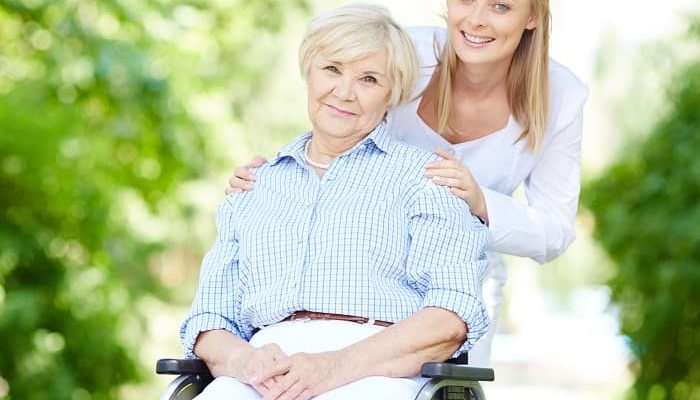 Frau im Rollstuhl wird von Ihrer Pflegerin im Park begleitet