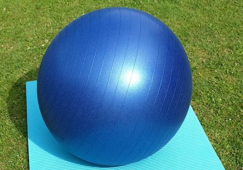 Ein großer blauer Gymnastikball liegt auf einer Yogamatte im Garten