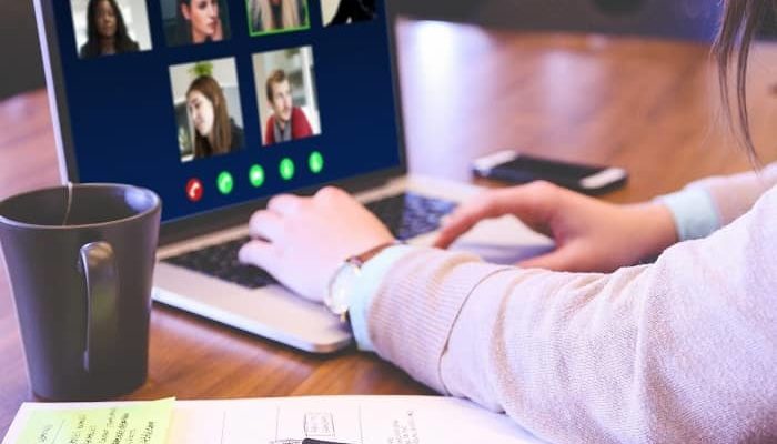 Frau sitzt vor einem Laptop und hat gerade eine Videokonferenz mit 5 Personen