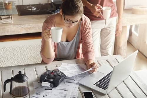 Junge Frau sitzt vor einem Laptop mit einer Tasse Kaffee und macht Buchhaltung