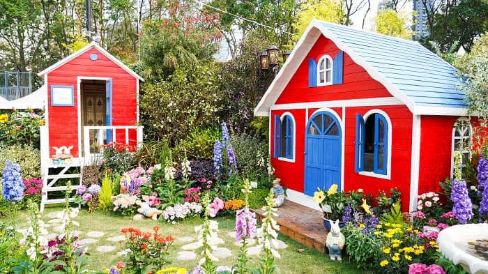 2 rote Gartenhäuschen stehen in einem bunten Blumengarten