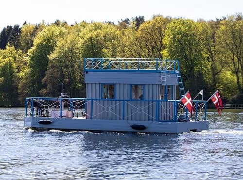 Ein kleines Hausboot mit verschiedenen Flaggen fährt auf einem Fluss