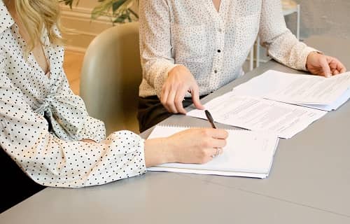 Zwei Frauen sitzen mit Papieren an einem Tisch und besprechen einen Text