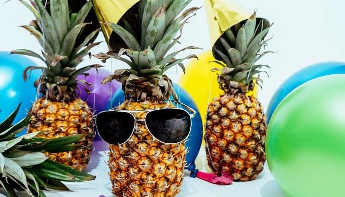 Eine Ananas mit Faschingshütchen, Luftballons und einer Sonnenbrille