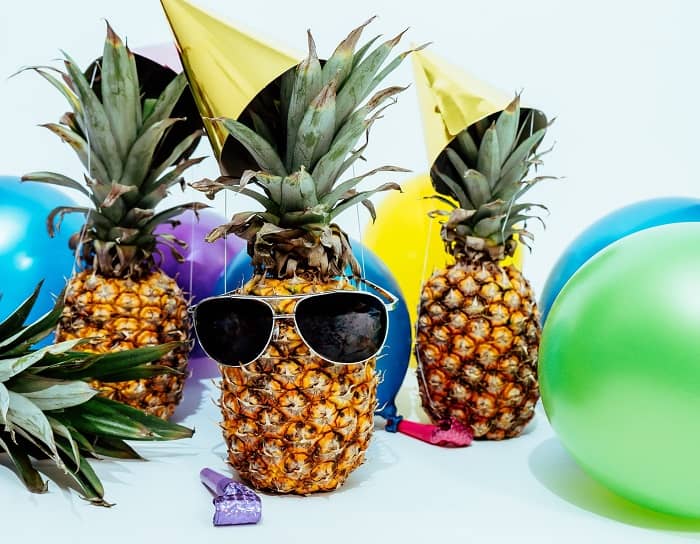 Eine Ananas mit Faschingshütchen, Luftballons und einer Sonnenbrille 