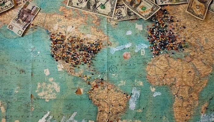 Auf einer Weltkarte sind viele Orte angepinnt und es liegen beschriftete Geldscheine, zu den jeweiligen Ländern mit Notizen, darauf