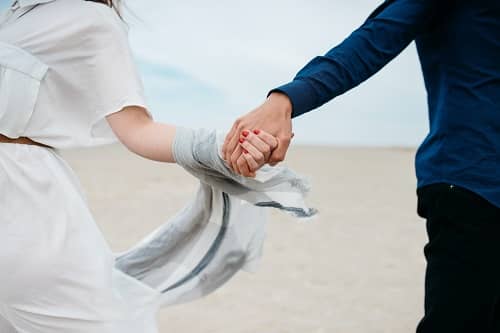 Ein Päärchen läuft Händehaltend über einen Strand.