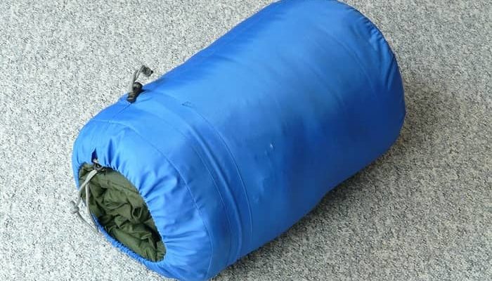 Ein Schlafsack in blauer Hülle liegt zusammengerollt am Boden