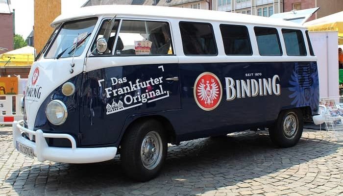 Ein dunkelblau/weißer VW-Bus mit großer Binding Bier Werbung