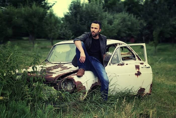 Ein Mann sitzt auf einem Schrottauto in mitten grüner Natur