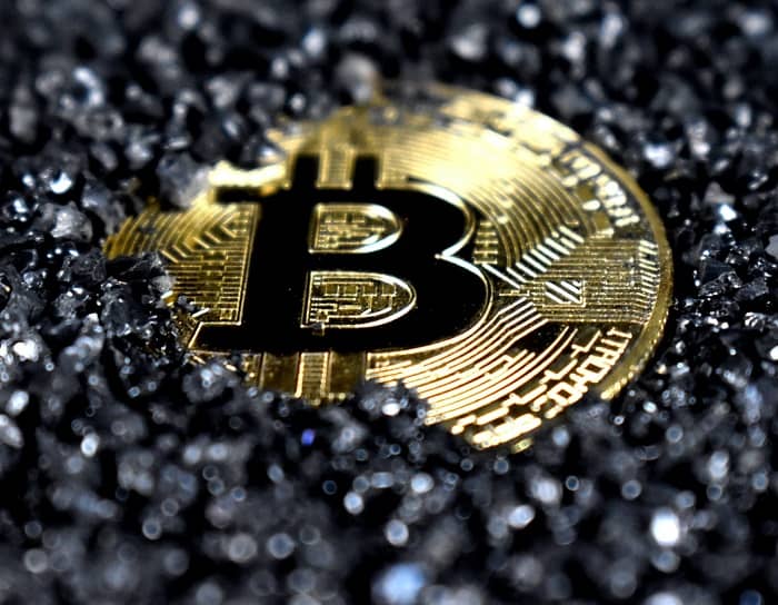 Eine Bitcoin Münze liegt in schwarzen Deco Steinen