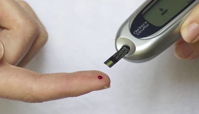 Ein Blutzuckertestgerät nimmt Blut auf von der Hand einer Frau