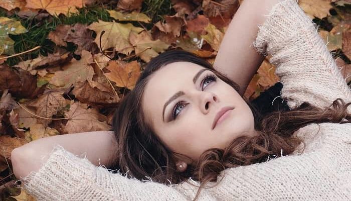 Eine junge, perfekt geschminkte Frau liegt im Herbstlaub